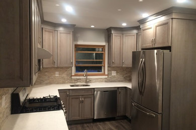 Cottage u-shaped medium tone wood floor open concept kitchen photo in New York with an undermount sink, shaker cabinets, distressed cabinets, solid surface countertops, gray backsplash, matchstick tile backsplash, stainless steel appliances and no island