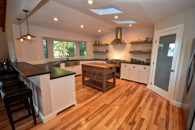 Example of an arts and crafts u-shaped light wood floor open concept kitchen design in Sacramento with shaker cabinets, white cabinets, solid surface countertops, an island, a farmhouse sink, white backsplash, subway tile backsplash and stainless steel appliances