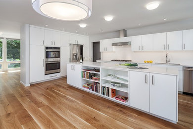 Example of a mid-sized minimalist u-shaped medium tone wood floor and brown floor open concept kitchen design in Portland with a double-bowl sink, flat-panel cabinets, white cabinets, granite countertops, white backsplash, stone tile backsplash, stainless steel appliances, an island and white countertops
