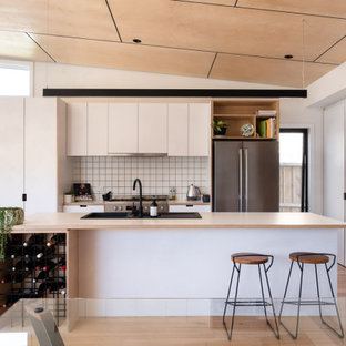 This is an example of a large contemporary open plan kitchen in Geelong with white cabinets, white splashback, ceramic splashback, stainless steel appliances, with island and beige benchtop.