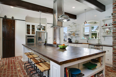 Enclosed kitchen - large traditional u-shaped brick floor and red floor enclosed kitchen idea in New Orleans with a farmhouse sink, glass-front cabinets, white cabinets, wood countertops, white backsplash, ceramic backsplash, white appliances and an island