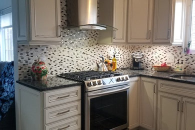 Eat-in kitchen - u-shaped eat-in kitchen idea in Milwaukee with a single-bowl sink, recessed-panel cabinets, beige cabinets, granite countertops, white backsplash, glass tile backsplash, stainless steel appliances, an island and black countertops