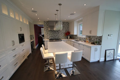 Large transitional u-shaped dark wood floor and brown floor open concept kitchen photo in Toronto with an undermount sink, shaker cabinets, white cabinets, quartz countertops, gray backsplash, glass tile backsplash, stainless steel appliances and an island