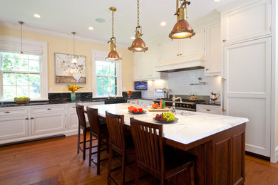 Large elegant l-shaped medium tone wood floor and brown floor enclosed kitchen photo in Boston with an integrated sink, recessed-panel cabinets, white cabinets, marble countertops, white backsplash, subway tile backsplash, paneled appliances and an island