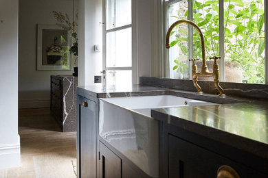 Klassisk inredning av ett litet brun brunt kök, med en rustik diskho, skåp i shakerstil, gröna skåp, brunt stänkskydd, stänkskydd i marmor, mellanmörkt trägolv och brunt golv