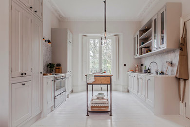 ロンドンにある広いトランジショナルスタイルのおしゃれなキッチン (シェーカースタイル扉のキャビネット、白いキャビネット、シルバーの調理設備、塗装フローリング、大理石カウンター) の写真