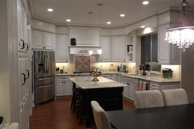 Eat-in kitchen - large traditional galley light wood floor eat-in kitchen idea in Phoenix with an undermount sink, raised-panel cabinets, white cabinets, granite countertops, beige backsplash, ceramic backsplash, stainless steel appliances and an island