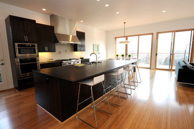 Modern l-shaped open plan kitchen in Seattle with a double-bowl sink, flat-panel cabinets, dark wood cabinets, stainless steel appliances, light hardwood flooring and an island.