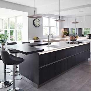 Photo of an expansive contemporary u-shaped eat-in kitchen in Surrey with an integrated sink, flat-panel cabinets, grey cabinets, mirror splashback, black appliances, porcelain floors, with island, grey floor and white benchtop.