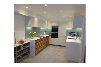 Inspiration for a small modern u-shaped kitchen/diner in Other with an integrated sink, grey cabinets, composite countertops, grey splashback, glass sheet splashback, black appliances and ceramic flooring.