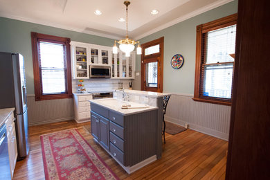 Mid-sized eclectic u-shaped light wood floor eat-in kitchen photo in Columbus with a drop-in sink, raised-panel cabinets, white cabinets, marble countertops, white backsplash, stone tile backsplash, stainless steel appliances and an island