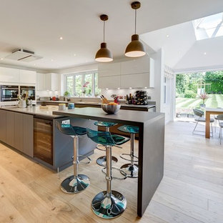 This is an example of a large contemporary kitchen/diner in London with flat-panel cabinets, light hardwood flooring, beige floors, white cabinets and stainless steel appliances.