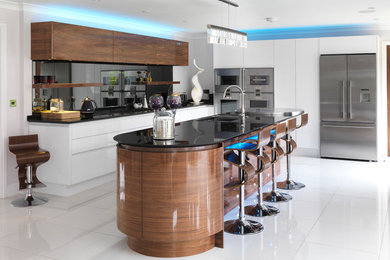 Large contemporary l-shaped open plan kitchen in Buckinghamshire with a double-bowl sink, flat-panel cabinets, dark wood cabinets, granite worktops, metallic splashback, mirror splashback, stainless steel appliances and an island.