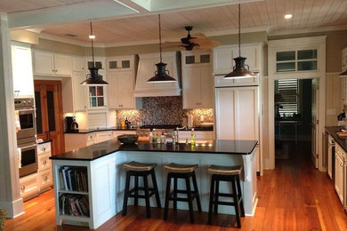 Example of a mid-sized transitional u-shaped medium tone wood floor and brown floor eat-in kitchen design in Miami with a farmhouse sink, recessed-panel cabinets, white cabinets, multicolored backsplash, stainless steel appliances and an island