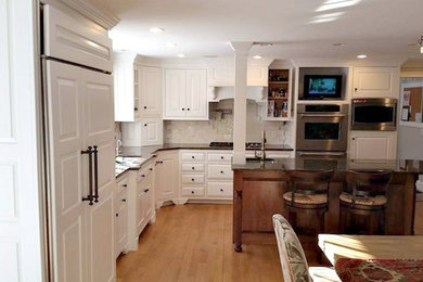 Example of a transitional l-shaped light wood floor eat-in kitchen design in Boston with an undermount sink, raised-panel cabinets, white cabinets, granite countertops, white backsplash, ceramic backsplash, stainless steel appliances and an island