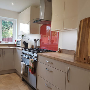 This is an example of a small contemporary u-shaped separate kitchen in West Midlands with a double-bowl sink, flat-panel cabinets, beige cabinets, laminate benchtops, orange splashback, glass sheet splashback, black appliances, vinyl floors, no island, brown floor and brown benchtop.