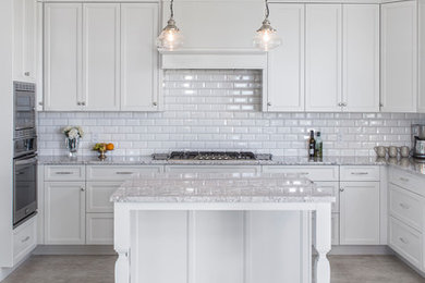 Mid-sized transitional u-shaped gray floor enclosed kitchen photo in Other with a double-bowl sink, shaker cabinets, white cabinets, white backsplash, subway tile backsplash, stainless steel appliances and an island