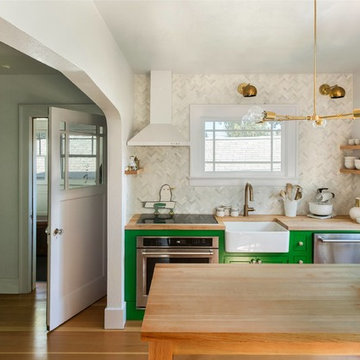 A large open concept kitchen with light wood floor, green shaker cabinets, a farmhouse sink, quartz countertops, red brick backsplash, paneled appliances, an island, and white countertops.