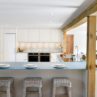 Photo of a large country u-shaped kitchen in Cornwall with a built-in sink, flat-panel cabinets, white cabinets, glass worktops, an island, blue worktops, multi-coloured splashback, stainless steel appliances, medium hardwood flooring and brown floors.