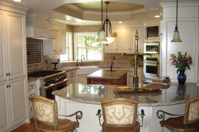 Example of a large classic u-shaped medium tone wood floor eat-in kitchen design in San Luis Obispo with a farmhouse sink, raised-panel cabinets, white cabinets, granite countertops, beige backsplash, stone tile backsplash, stainless steel appliances and an island
