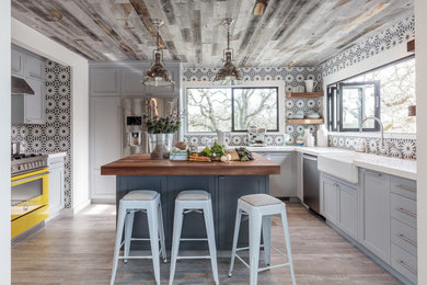 Example of a transitional u-shaped light wood floor kitchen design in San Francisco with a farmhouse sink, shaker cabinets, multicolored backsplash, ceramic backsplash, colored appliances, an island and blue cabinets
