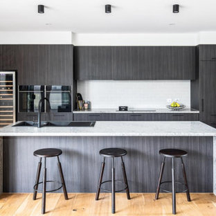Photo of a large contemporary galley kitchen in Melbourne with a double-bowl sink, flat-panel cabinets, dark wood cabinets, white splashback, subway tile splashback, panelled appliances, light hardwood floors, with island, beige floor and grey benchtop.