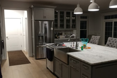 Photo of a medium sized contemporary single-wall kitchen pantry in Philadelphia with stainless steel appliances, an island, a belfast sink, shaker cabinets, grey cabinets, soapstone worktops, light hardwood flooring and brown floors.