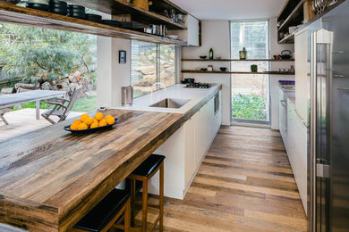 Cette image montre une petite cuisine parallèle design avec un évier encastré, des portes de placard blanches, un plan de travail en bois, un électroménager en acier inoxydable, un sol en bois brun et un placard à porte plane.
