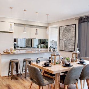 Photo of a contemporary galley eat-in kitchen in Other with a double-bowl sink, flat-panel cabinets, white cabinets, mirror splashback, white appliances, medium hardwood floors, with island, brown floor and grey benchtop.