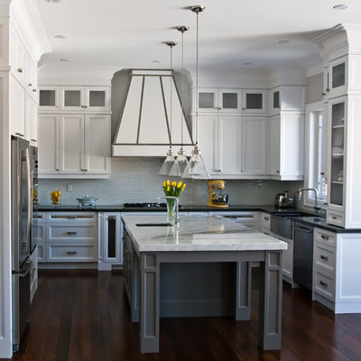 Large transitional u-shaped medium tone wood floor kitchen photo in Toronto with a farmhouse sink, recessed-panel cabinets, white cabinets, gray backsplash, glass tile backsplash, stainless steel appliances and an island