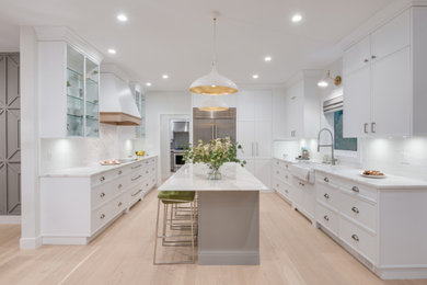 Eat-in kitchen - large transitional u-shaped light wood floor and beige floor eat-in kitchen idea with a farmhouse sink, white cabinets, white backsplash, an island, white countertops, flat-panel cabinets, quartz countertops and stainless steel appliances