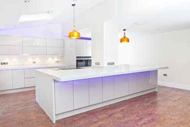 Large contemporary open plan kitchen in Buckinghamshire with an integrated sink, flat-panel cabinets, composite countertops, stainless steel appliances, vinyl flooring and an island.