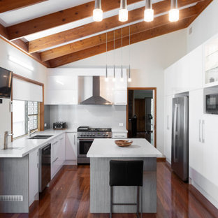 Photo of a contemporary u-shaped kitchen in Brisbane with a drop-in sink, flat-panel cabinets, white cabinets, stainless steel appliances, dark hardwood floors, with island, brown floor and white benchtop.
