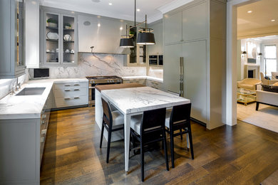 Example of a trendy u-shaped medium tone wood floor and brown floor kitchen design in Chicago with gray cabinets, paneled appliances, an island, an undermount sink, glass-front cabinets, white backsplash and white countertops
