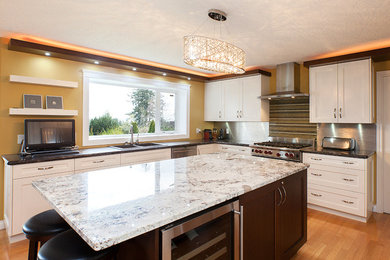 Photo of a large classic u-shaped open plan kitchen in Vancouver with a double-bowl sink, shaker cabinets, white cabinets, granite worktops, metallic splashback, metal splashback, stainless steel appliances, light hardwood flooring, an island and brown floors.