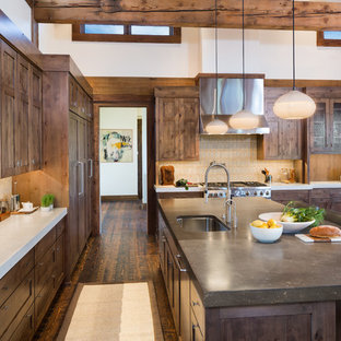 Modelo de cocina rural con fregadero bajoencimera, armarios estilo shaker, puertas de armario de madera en tonos medios, salpicadero multicolor, electrodomésticos de acero inoxidable, suelo de madera oscura y una isla
