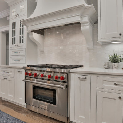 Inspiration for a large timeless u-shaped light wood floor and multicolored floor eat-in kitchen remodel in Boston with a farmhouse sink, beaded inset cabinets, white cabinets, quartz countertops, white backsplash, marble backsplash, stainless steel appliances, an island and white countertops