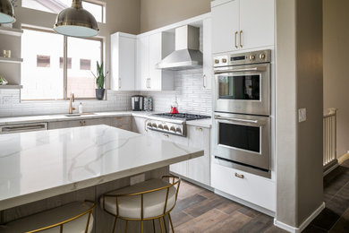 Trendy l-shaped laminate floor and brown floor eat-in kitchen photo in Phoenix with a single-bowl sink, white cabinets, marble countertops, white backsplash, ceramic backsplash, stainless steel appliances, an island, white countertops and flat-panel cabinets