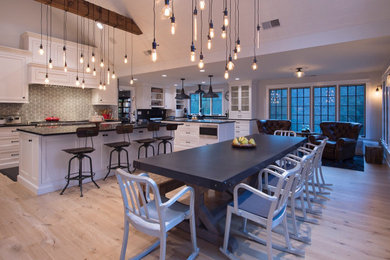 Example of a large transitional u-shaped light wood floor and beige floor eat-in kitchen design with shaker cabinets, white cabinets, multicolored backsplash, ceramic backsplash, two islands and black countertops