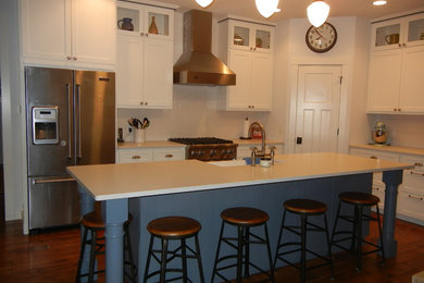 Example of a mid-sized transitional l-shaped medium tone wood floor and red floor enclosed kitchen design in Cedar Rapids with a farmhouse sink, recessed-panel cabinets, white cabinets, quartz countertops, white backsplash, subway tile backsplash, stainless steel appliances and an island