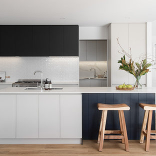 This is an example of a contemporary kitchen in Hobart with an undermount sink, flat-panel cabinets, white cabinets, white splashback, stainless steel appliances, light hardwood floors, with island and white benchtop.