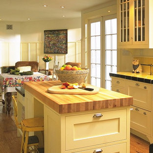 This is an example of a mid-sized traditional u-shaped eat-in kitchen in San Francisco with a farmhouse sink, white cabinets, tile benchtops, yellow splashback, ceramic splashback, stainless steel appliances, medium hardwood floors, with island, shaker cabinets and yellow benchtop.