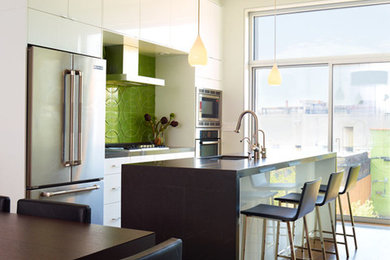 Photo of a medium sized contemporary galley open plan kitchen in New York with a submerged sink, flat-panel cabinets, white cabinets, composite countertops, green splashback, ceramic splashback, stainless steel appliances, dark hardwood flooring and an island.