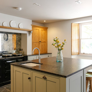 Rustic l-shaped kitchen in Cornwall with a submerged sink, shaker cabinets, green cabinets, mirror splashback, black appliances, an island and black worktops.