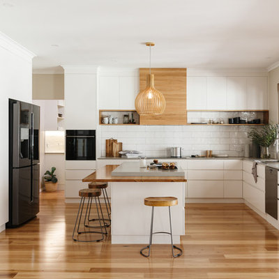 Example of a trendy l-shaped medium tone wood floor and beige floor open concept kitchen design in Adelaide with an undermount sink, flat-panel cabinets, white cabinets, white backsplash, white appliances and an island