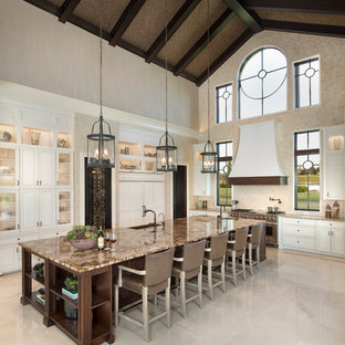 Ejemplo de cocina comedor larga, mediterránea, extra grande, con fregadero sobremueble, puertas de armario blancas, encimera de granito, salpicadero de piedra caliza, electrodomésticos con paneles, suelo de mármol, una isla, salpicadero beige, suelo beige y armarios tipo vitrina