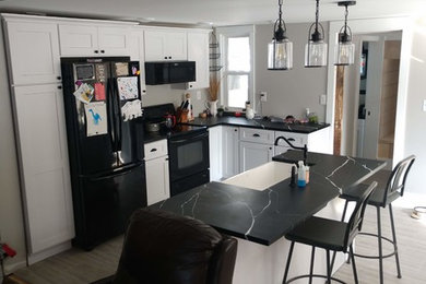 Example of a mid-sized arts and crafts l-shaped vinyl floor and gray floor eat-in kitchen design in Grand Rapids with a farmhouse sink, shaker cabinets, white cabinets, solid surface countertops, black appliances, an island and black countertops