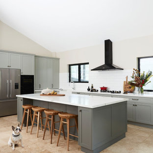 Aménagement d'une grand cuisine américaine classique en L avec un évier de ferme, un placard à porte shaker, des portes de placards vertess, un plan de travail en quartz modifié, une crédence blanche, une crédence en carreau de céramique, un électroménager noir, un sol en travertin, un îlot central, un sol jaune et un plan de travail blanc.