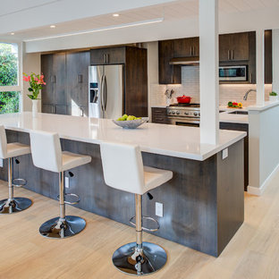 Foto di una cucina moderna di medie dimensioni con lavello sottopiano, ante lisce, top in quarzo composito, elettrodomestici in acciaio inossidabile, isola, top bianco, ante in legno bruno, paraspruzzi bianco, parquet chiaro e pavimento beige