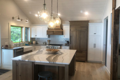 Huge beach style l-shaped medium tone wood floor and brown floor eat-in kitchen photo in Other with a farmhouse sink, recessed-panel cabinets, white cabinets, granite countertops, white backsplash, subway tile backsplash, stainless steel appliances, an island and gray countertops